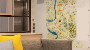 A hotel lobby with a map on the wall, an elevator, and a couch with a pillow.