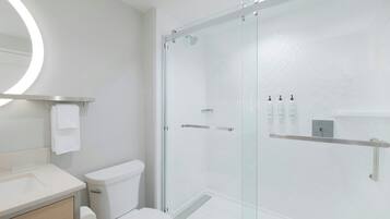 Un baño moderno con ducha de vidrio, inodoro, lavamanos y espejo con luz circular.