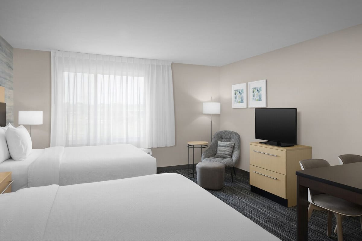 Una habitación de hotel con dos camas, televisión, escritorio y silla.