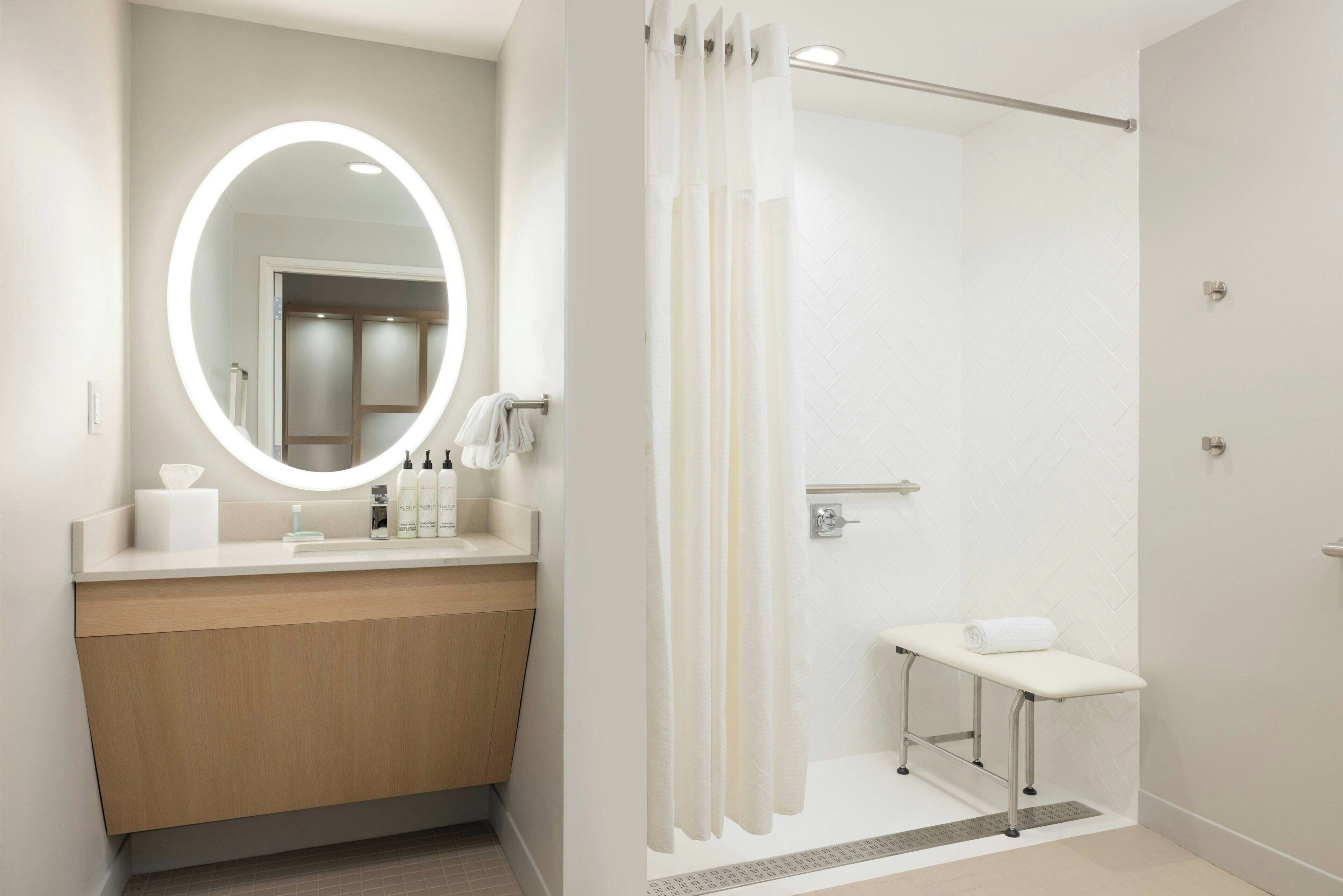 A modern bathroom with a vanity, mirror, shower, and bench.