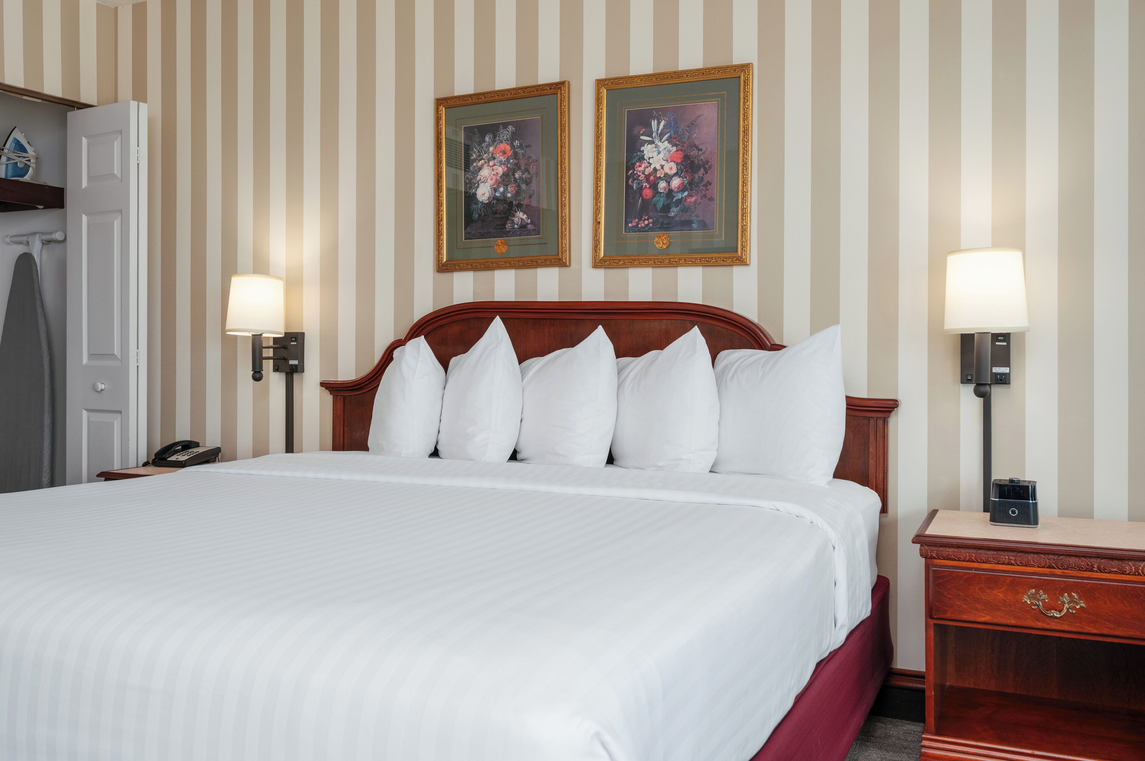 Una camera d'albergo con un letto grande, due lampade a parete, un comodino in legno e due quadri floreali incorniciati.