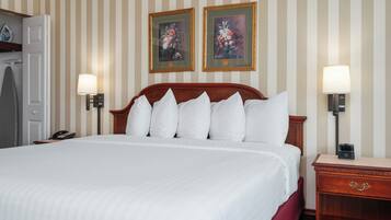 Una camera d'albergo con un letto grande, due lampade a parete, un comodino in legno e due quadri floreali incorniciati.
