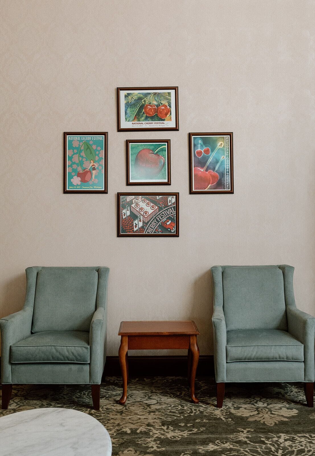 A room with two armchairs, a small wooden table, and four framed posters on the wall.