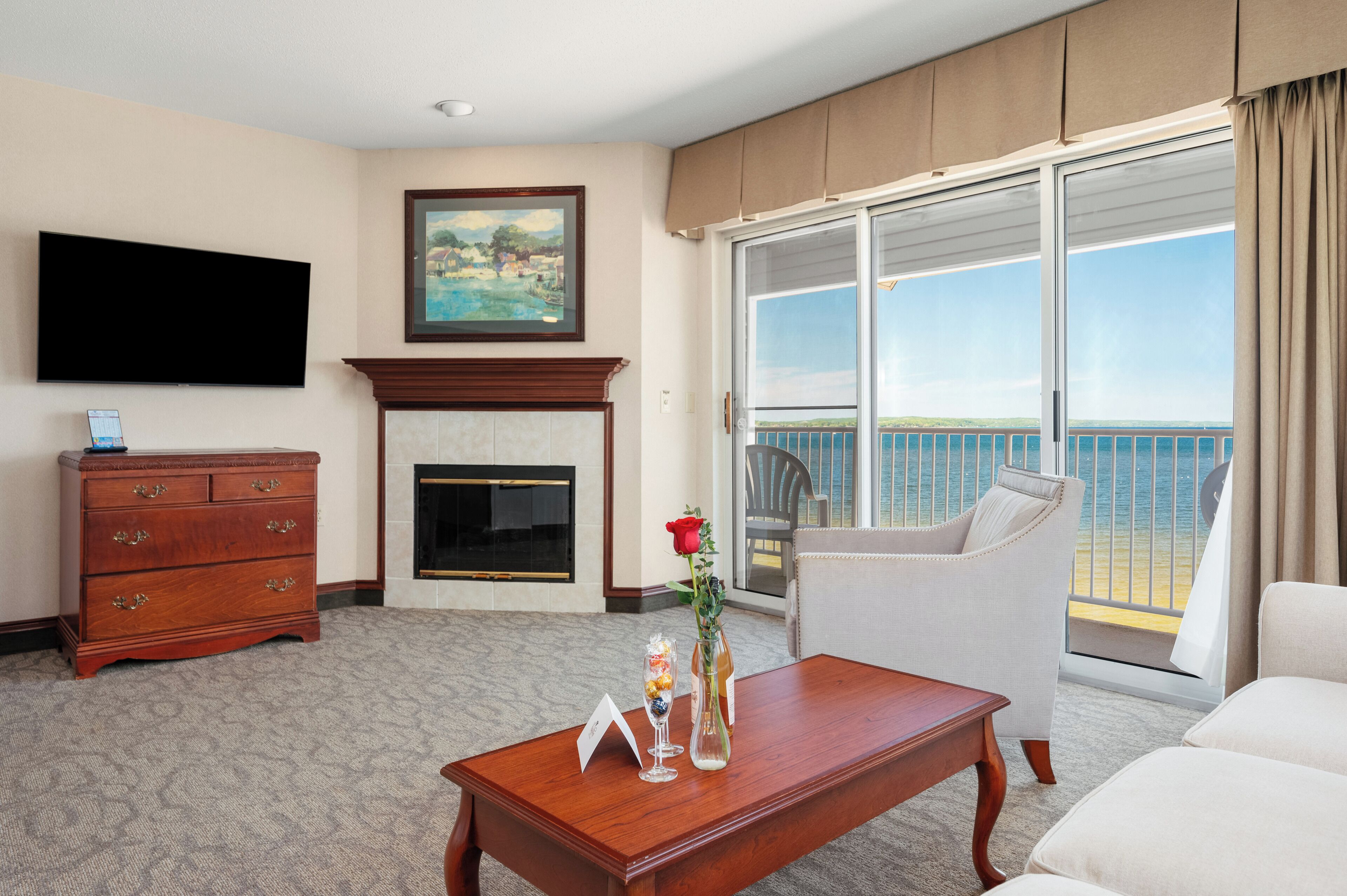 Een hotelkamer met een open haard, een flatscreen-televisie, een eettafel, een bank en een balkon met uitzicht op zee.