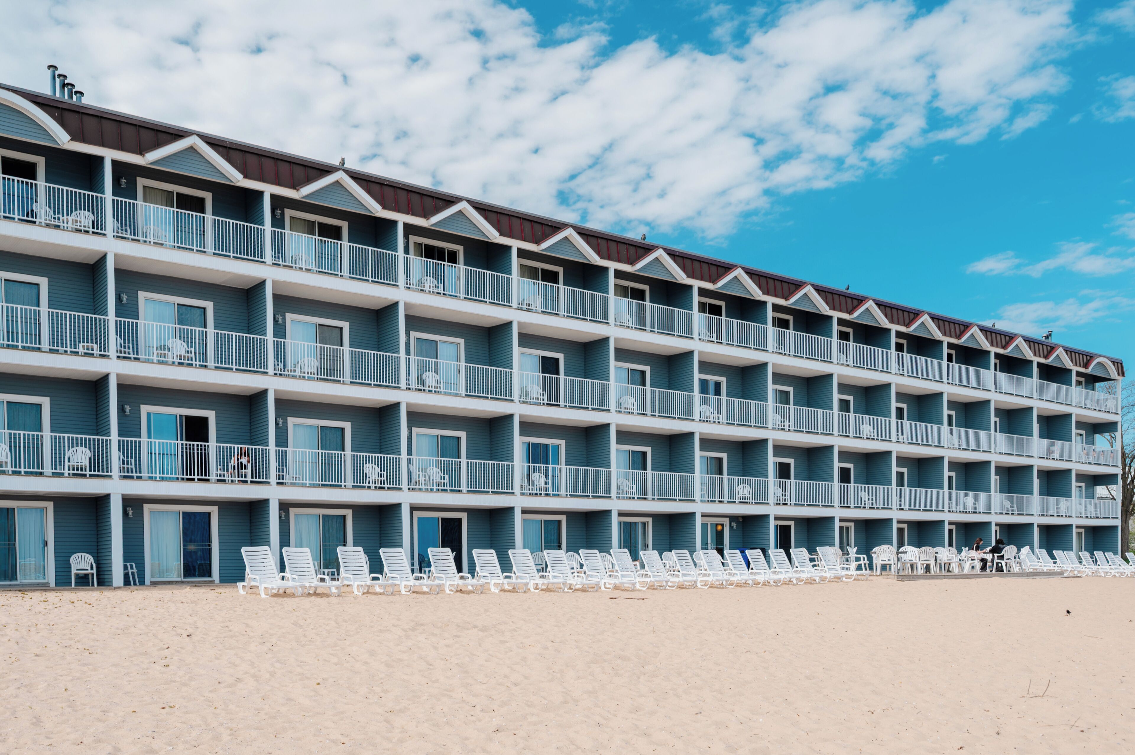 A multi-story hotel with balconies, beachside lounge chairs, and a clear sky.