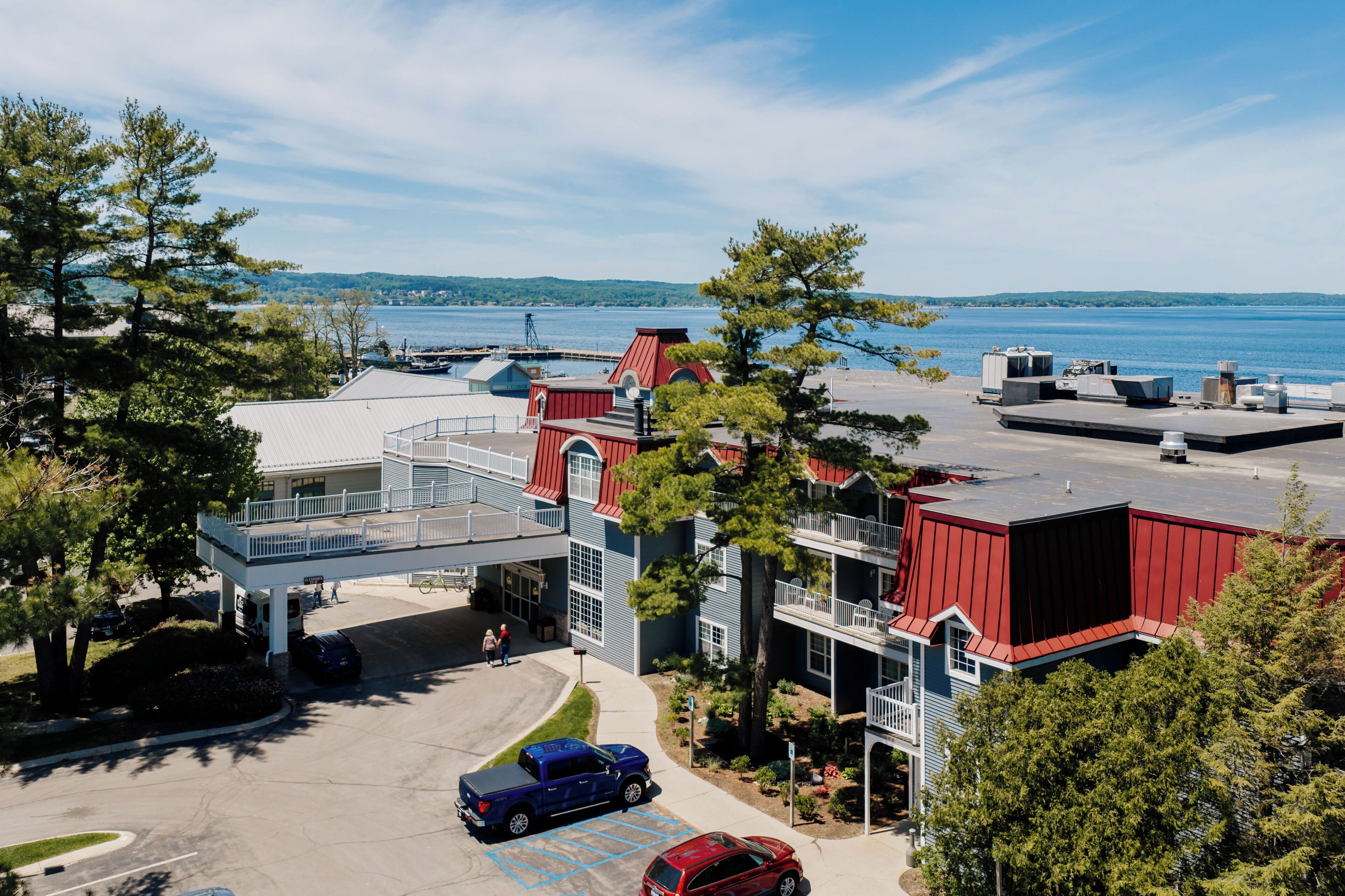 A multi-story building with a red roof, a covered parking area, and a view of a body of water.