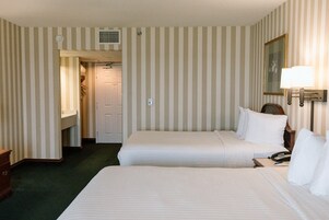 Habitación de hotel con dos camas, un escritorio con teléfono, una lámpara y una puerta que da a un pasillo.