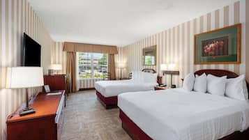 A hotel room with two beds, a desk, a TV, and a window with a view of buildings.