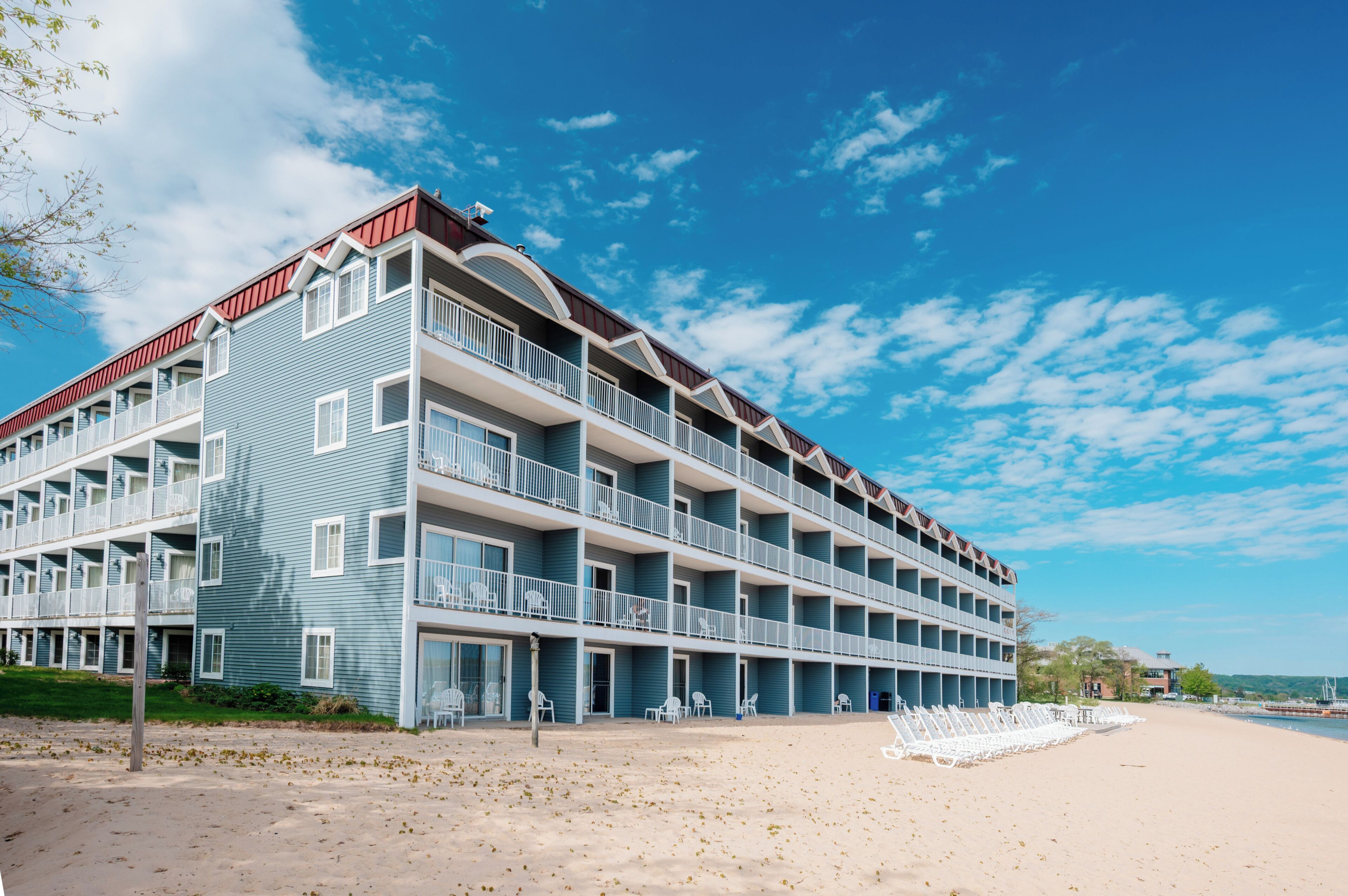 Ein mehrstöckiges Hotel mit Balkonen, ein Sandstrand davor und ein klarer, blauer Himmel.