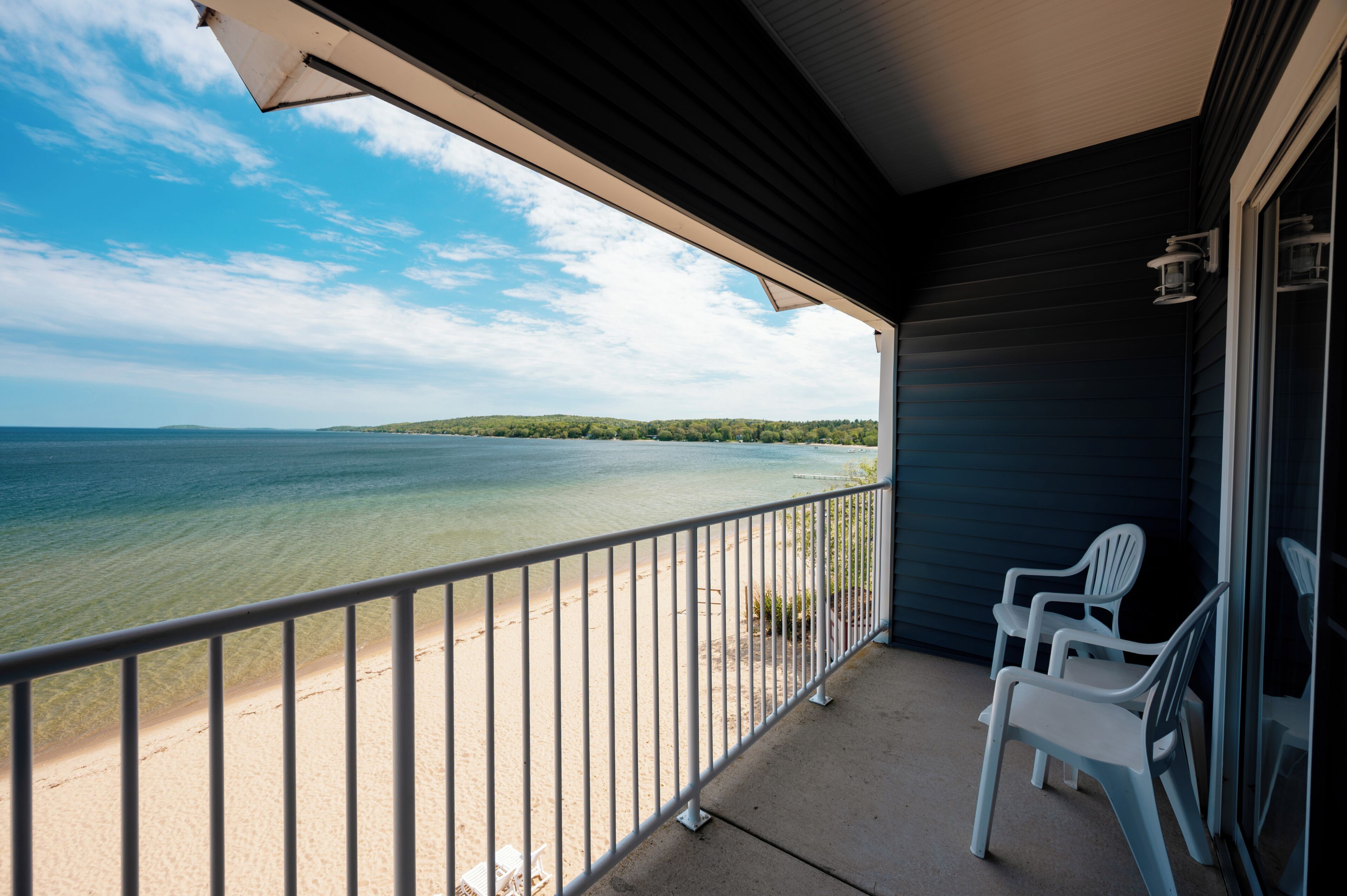 Ein Balkon mit Blick auf Strand und See, zwei weiße Plastikstühle und ein Geländer.