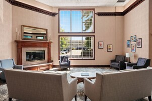 A room with a fireplace, two armchairs, a coffee table, and a large window with a view of the outside.