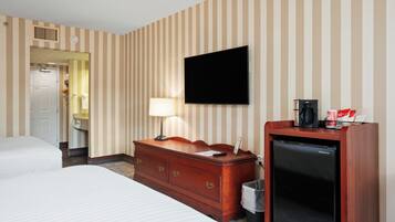 A hotel room with striped wallpaper, a flat-screen TV, a wooden dresser, a mini fridge, and a bed.
