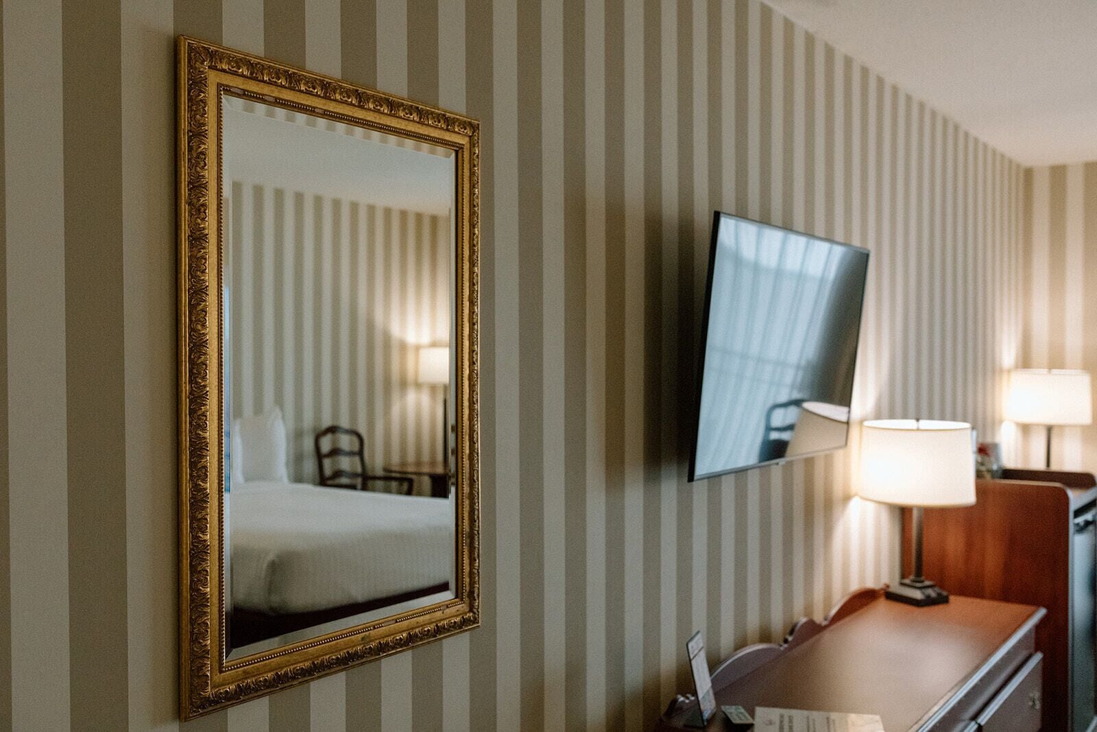 Une chambre d’hôtel avec un lit, un bureau doté d’une lampe et un téléviseur fixé au mur.