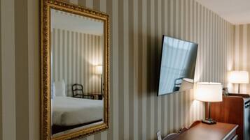 Une chambre d’hôtel avec un lit, un bureau doté d’une lampe et un téléviseur fixé au mur.