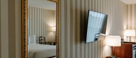 A hotel room with a bed, a desk with a lamp, and a TV mounted on the wall.