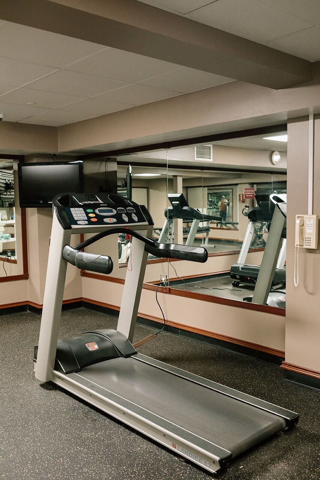 A gym with a treadmill, a mirrored wall, and a phone on the wall.