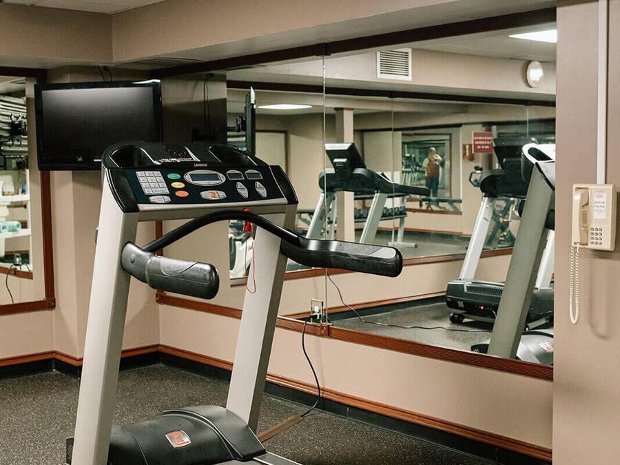 A gym with a treadmill, a mirrored wall, and a phone on the wall.