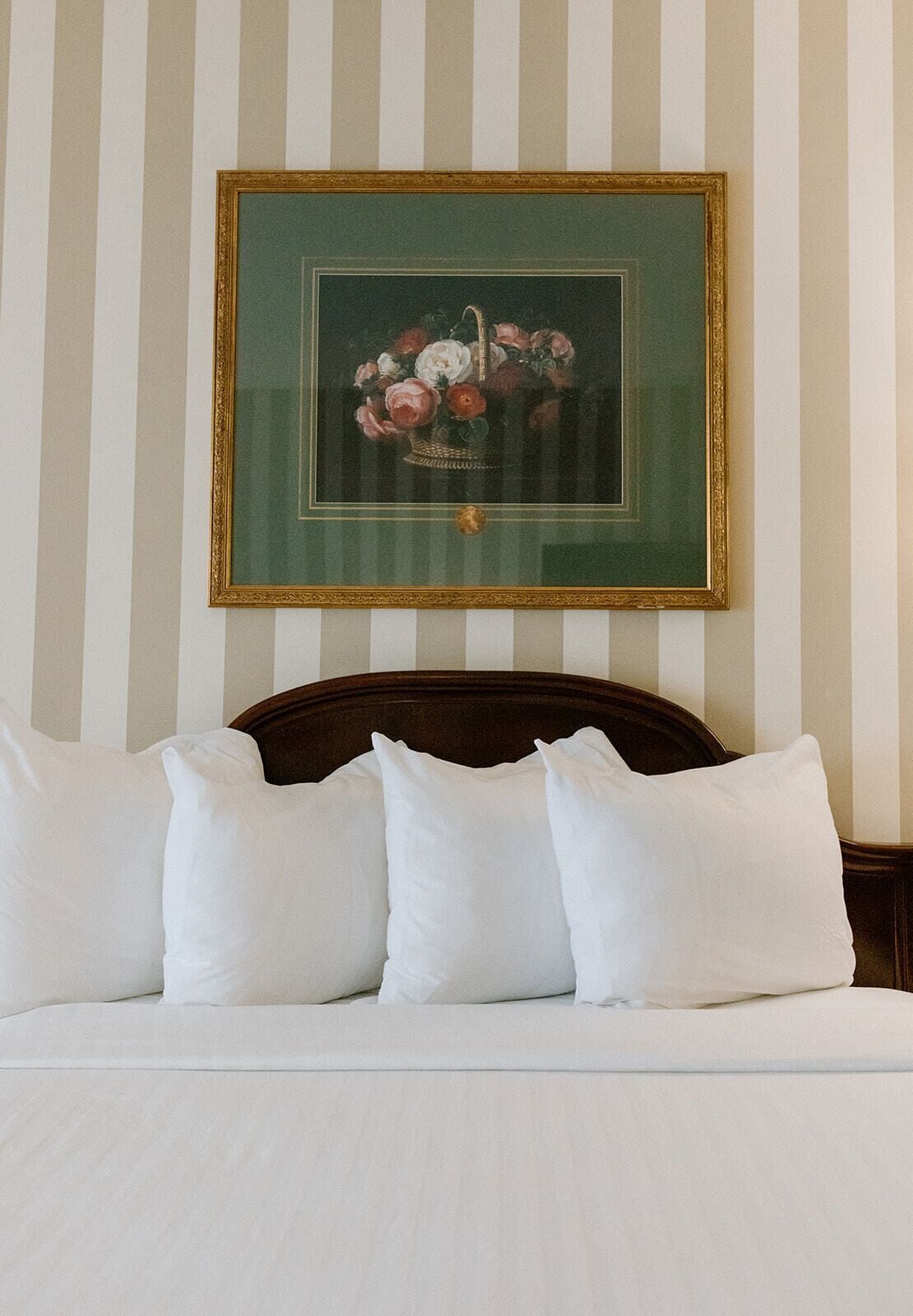 A neatly made bed with white pillows and a framed floral artwork above it.