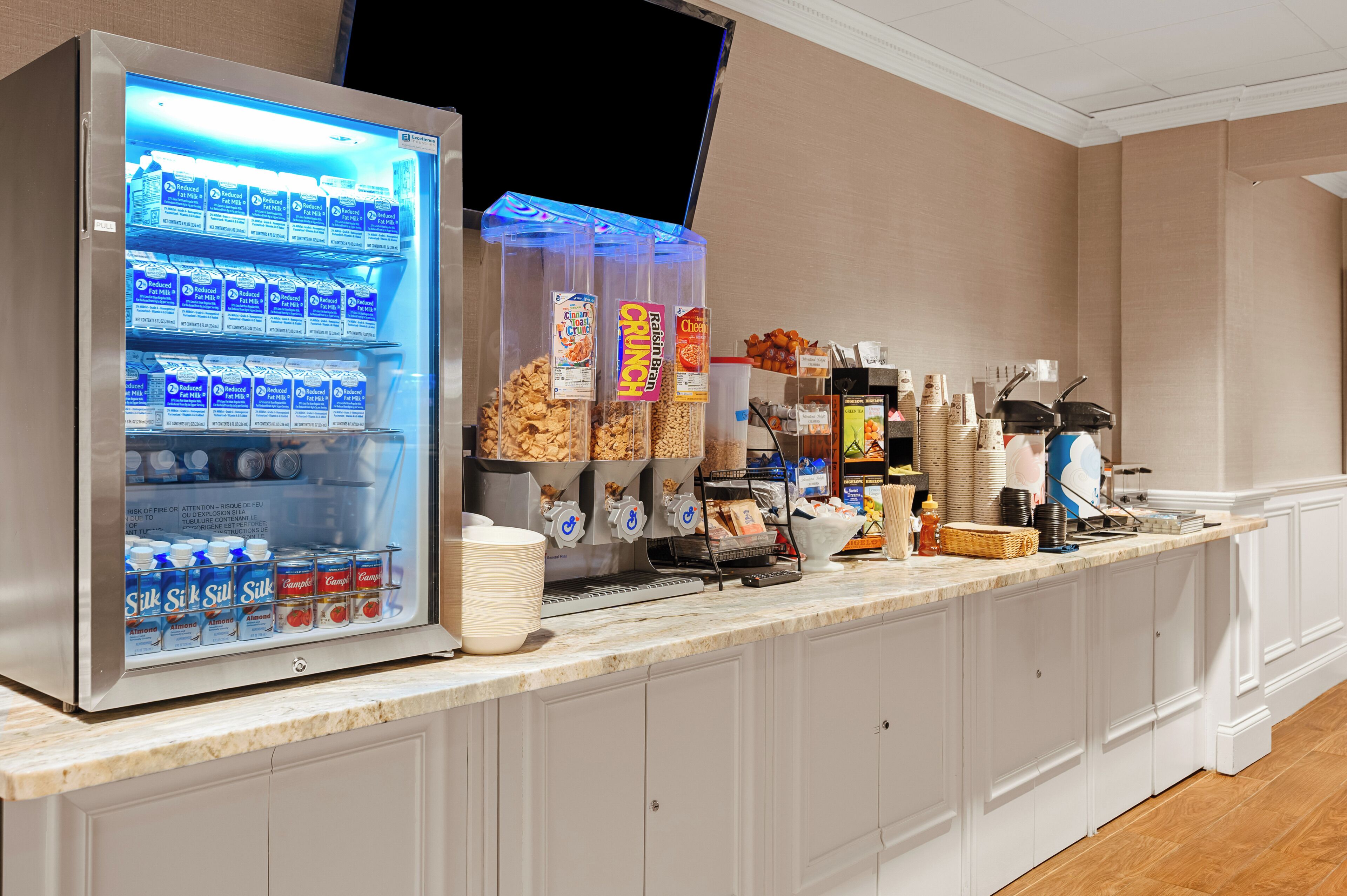 A self-service breakfast bar with a refrigerator stocked with milk, cereal, and beverages.