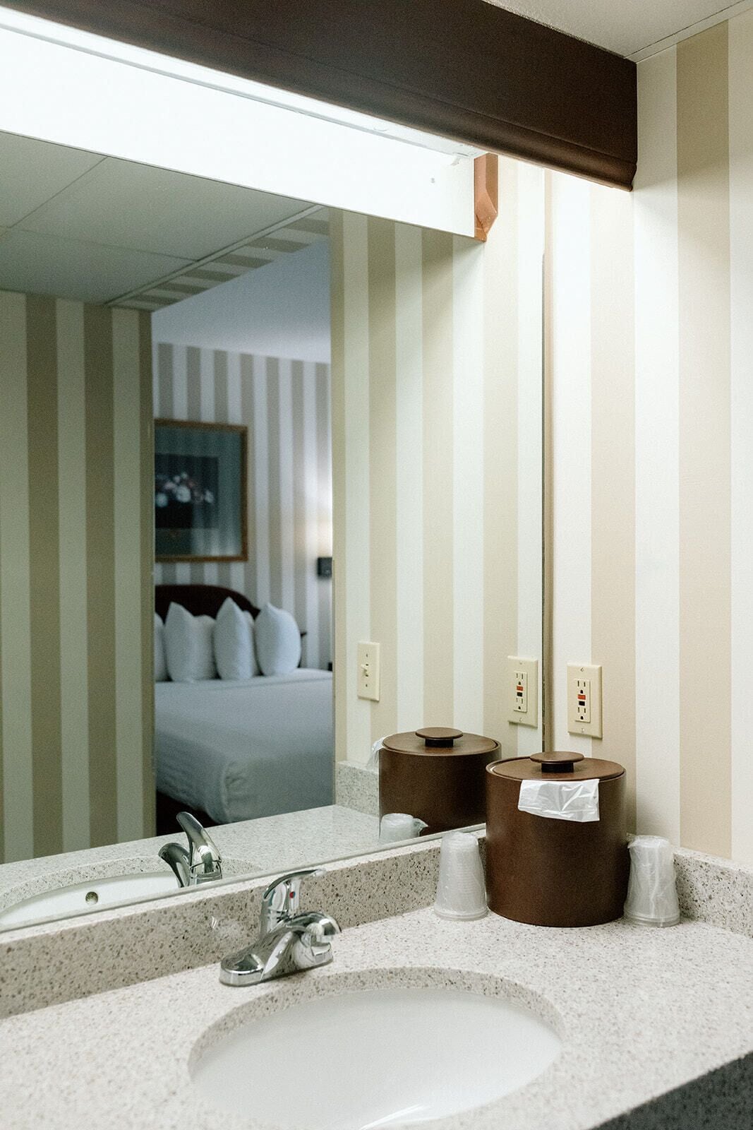 A hotel bathroom with a large mirror, a sink, and two trash bins.