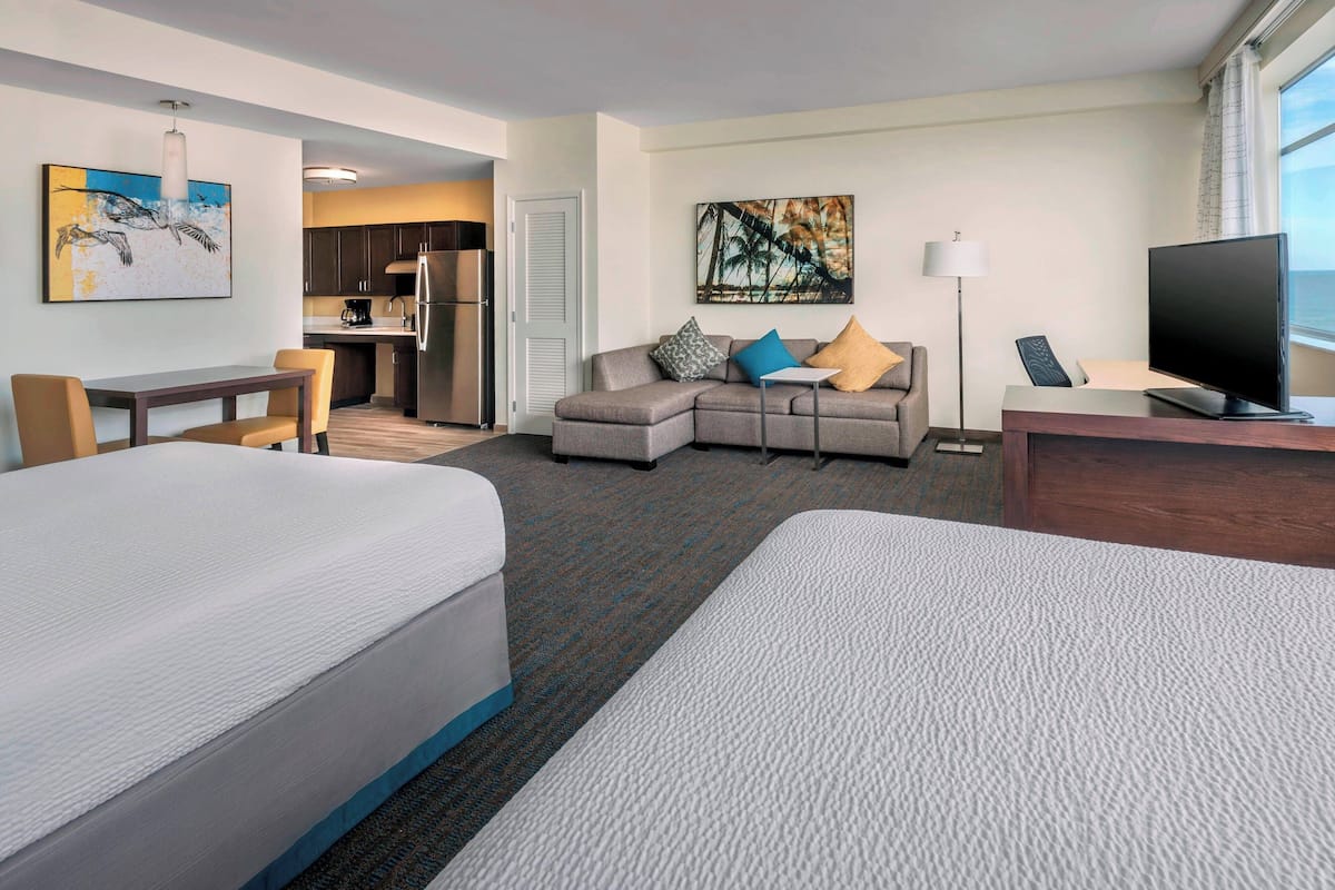 A hotel room with two beds, a sofa, a desk, a television, and artwork on the walls.