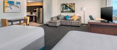 A hotel room with two beds, a sofa, a desk, a television, and artwork on the walls.