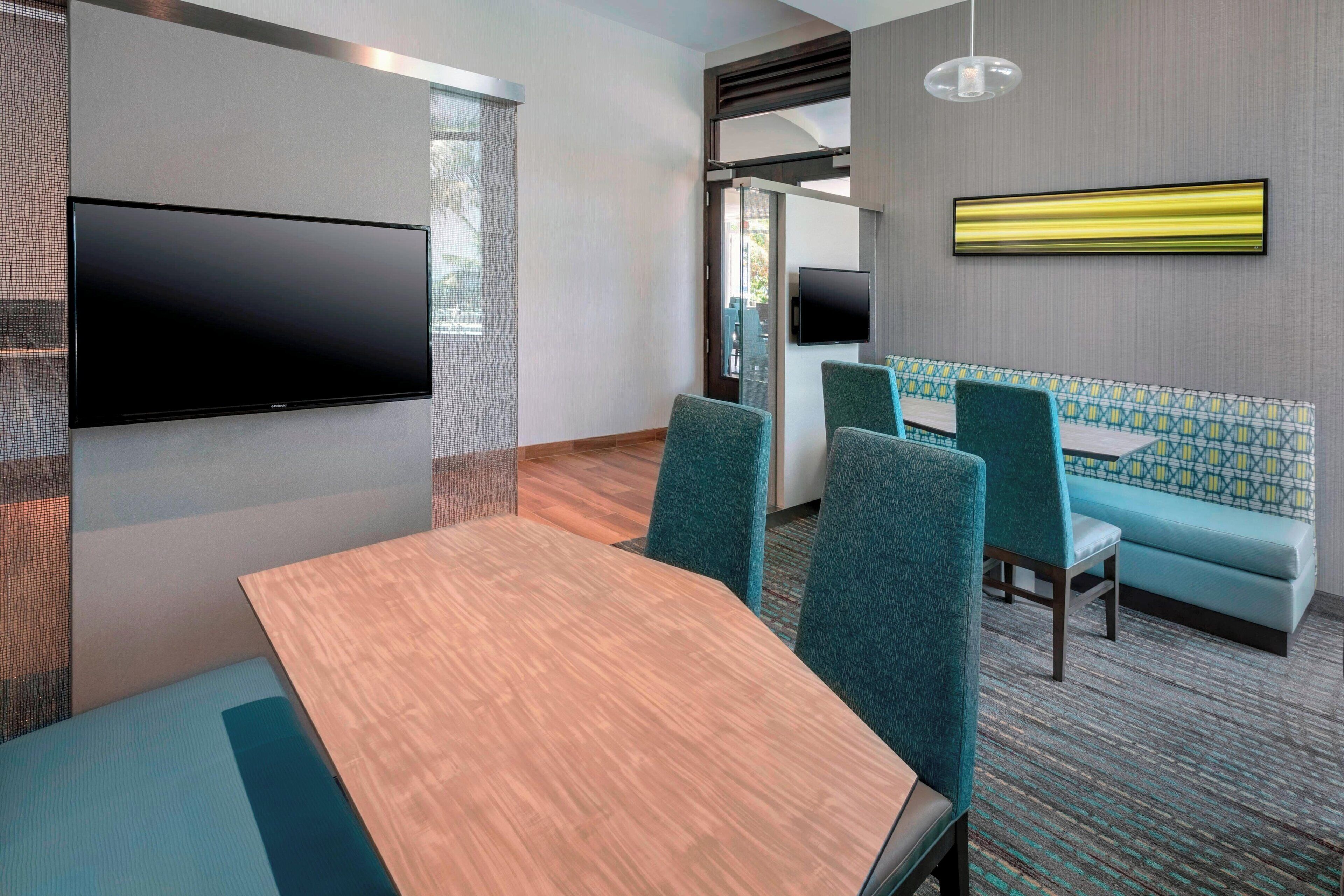 Une salle de conférence moderne équipée d’un grand téléviseur à écran plat, d’une table en bois, de chaises de couleur turquoise et d’un canapé à motifs.
