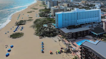Um hotel à beira-mar com um edifício grande, uma praia e uma piscina.