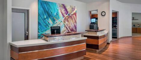 A reception desk with a modern design, a large abstract painting on the wall, and a clock above it.