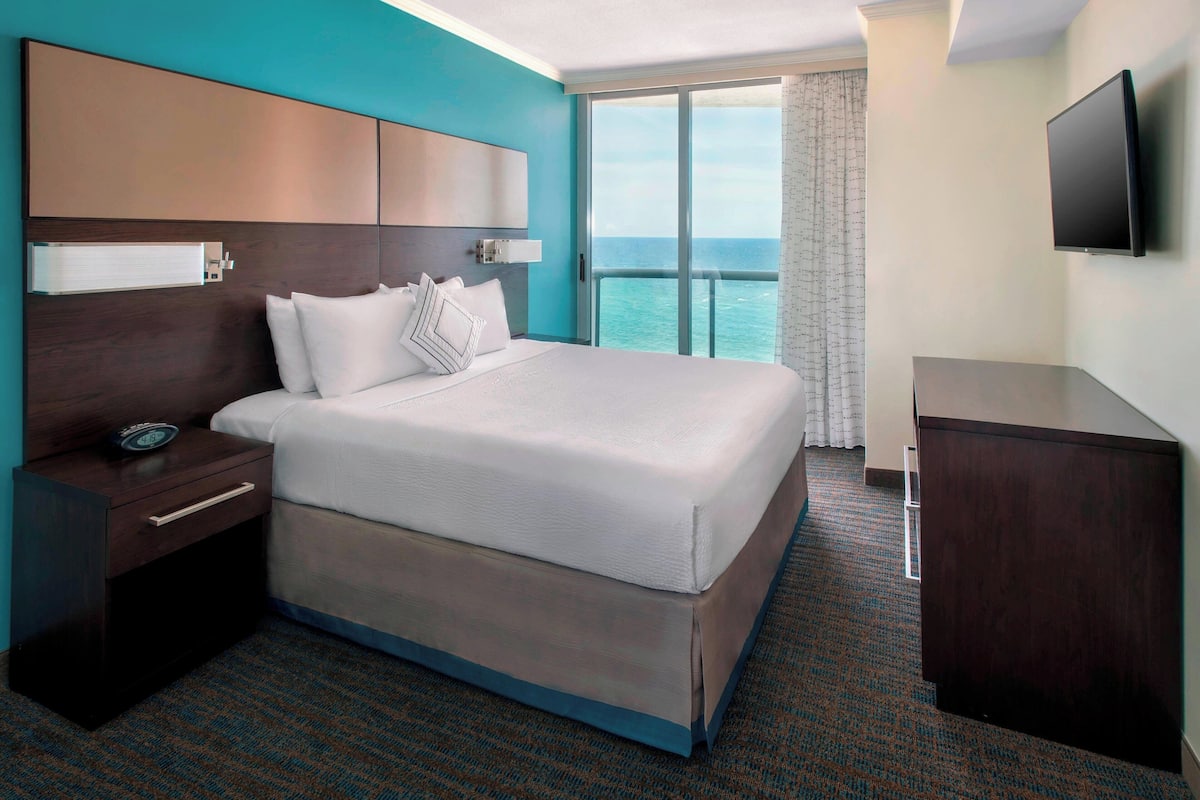 A hotel room with a large bed, a nightstand, a dresser, and a TV mounted on the wall.