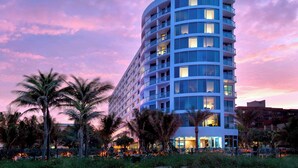 A modern hotel with multiple balconies, surrounded by palm trees and a fence. - Residence Inn Fort Lauderdale Pompano Beach / Oceanfront (Pompano Beach)