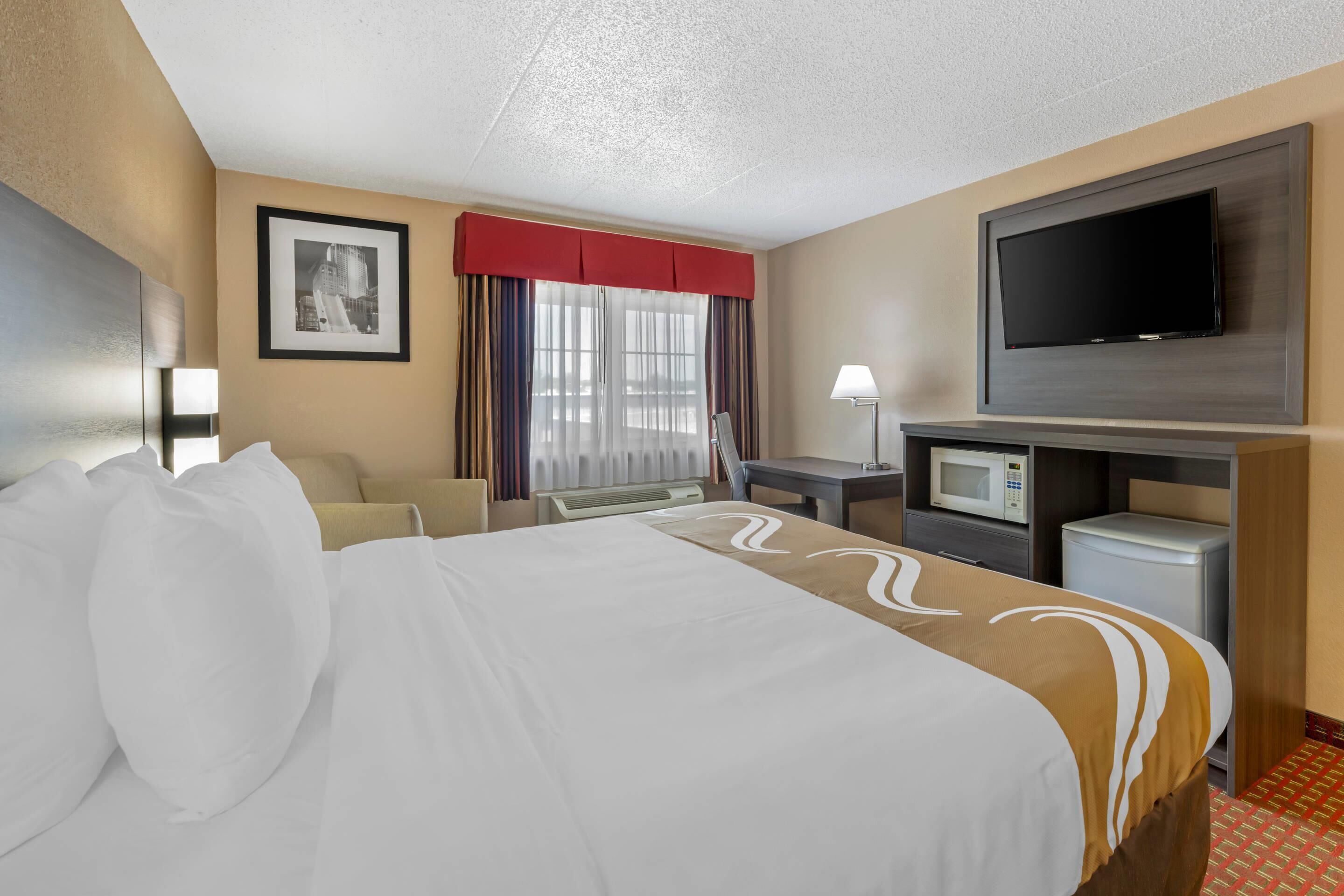 A hotel room with a bed, a desk, a television, and a microwave.
