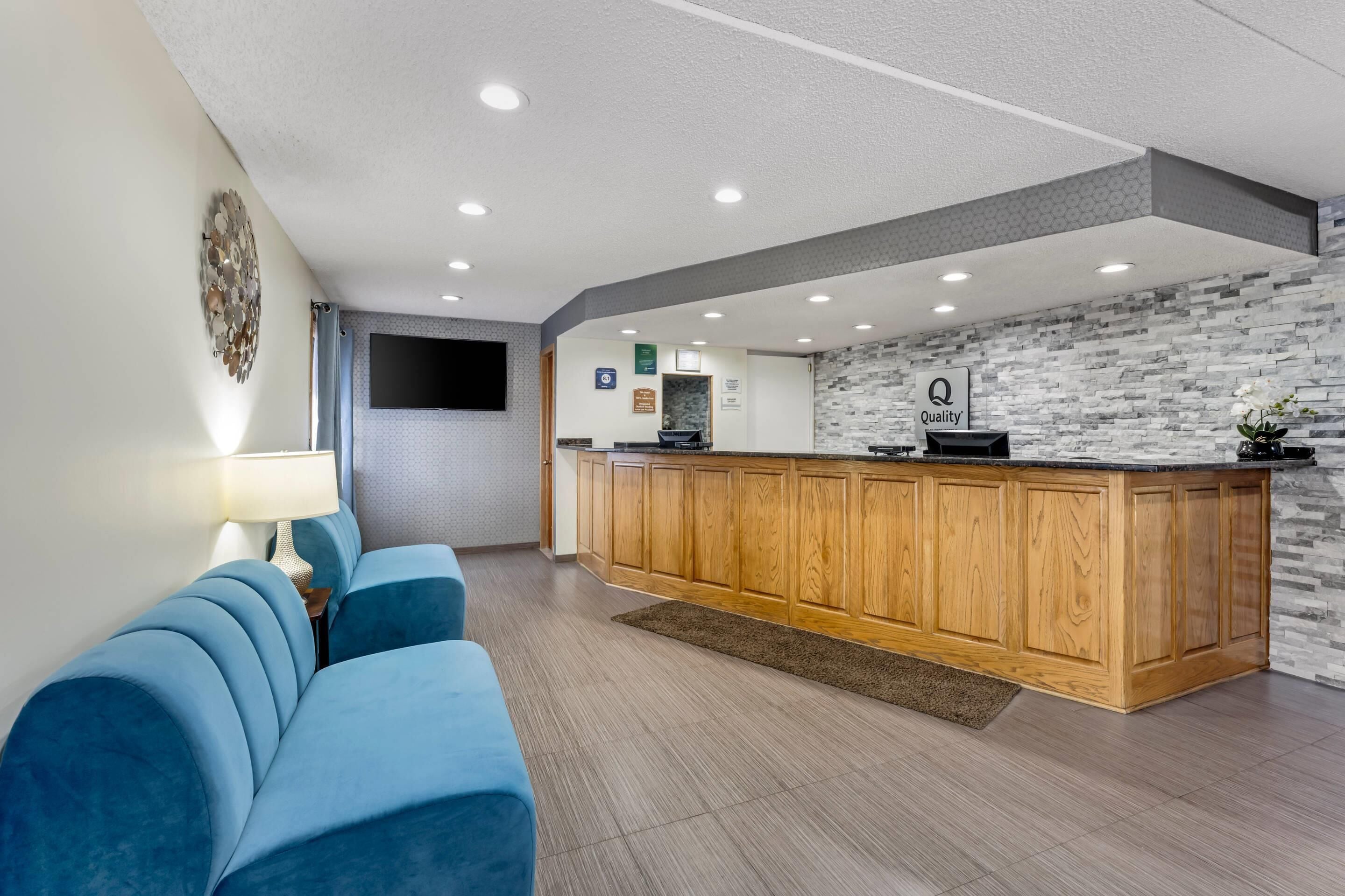 A hotel lobby with a blue sofa, wooden reception desk, and a stone-patterned wall.