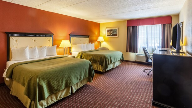 A hotel room with two beds, a desk, a chair, a television, and a window with curtains. - Quality Inn & Suites Lincoln South (Lincoln)