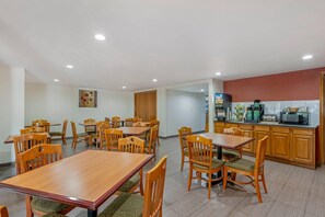 A dining area with wooden tables and chairs, a kitchen with appliances, and a painting on the wall. - Quality Inn & Suites Lincoln South (Lincoln)