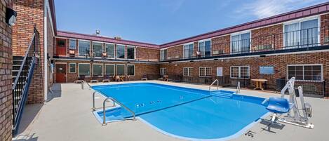 Una piscina con tabla de clavados y sillas de descanso, rodeada de edificios de ladrillo con ventanas amplias y balcones.