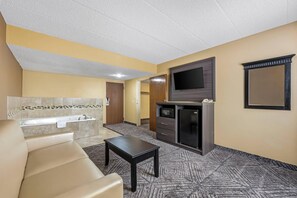 A hotel room with a sofa, a small table, a flat-screen TV, a minibar, and a bathroom with a bathtub. - Quality Inn & Suites Lincoln South (Lincoln)