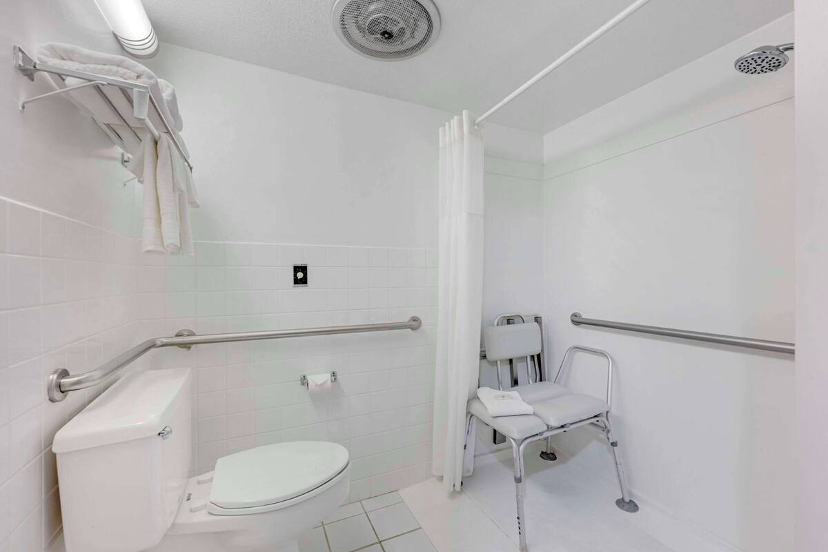 A modern bathroom with a toilet, a shower with a handheld showerhead, and a grab bar near the sink.