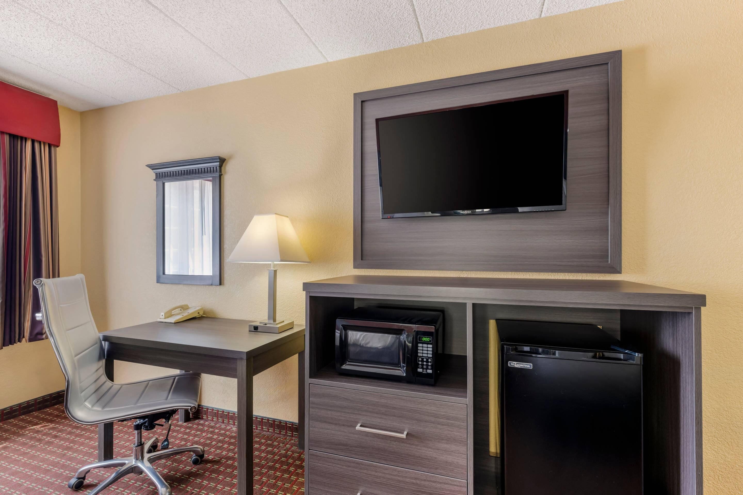 A hotel room with a desk, chair, television, lamp, microwave, and a telephone.