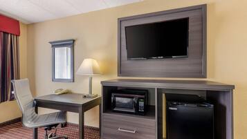 A hotel room with a desk, chair, television, lamp, microwave, and a telephone.