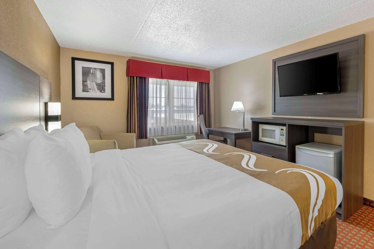 A hotel room with a large bed, a desk, a television, and a microwave.