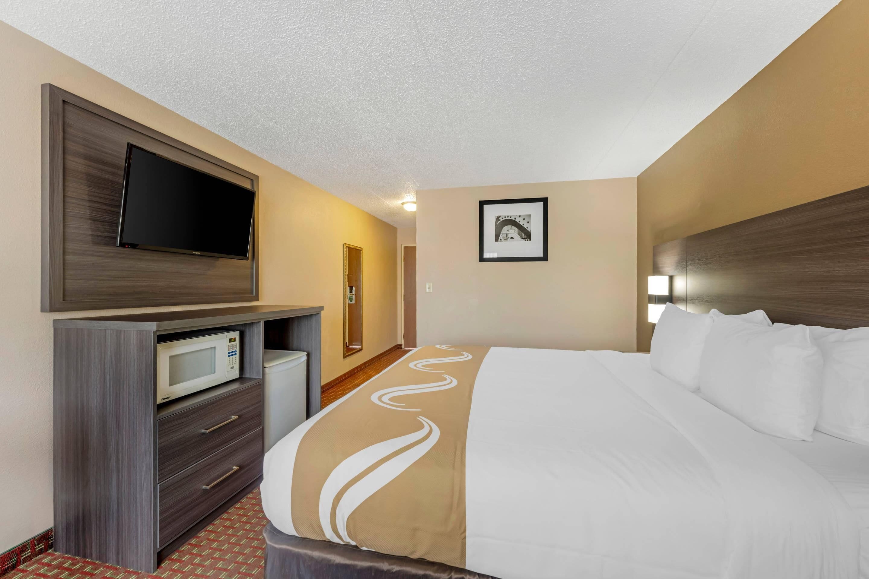 Habitación de hotel con cama, televisor de pantalla plana en la pared, microondas y un mueble pequeño.