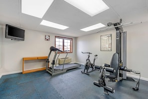 A gym with exercise equipment, a bench, a clock, and a window. - Quality Inn & Suites Lincoln South (Lincoln)