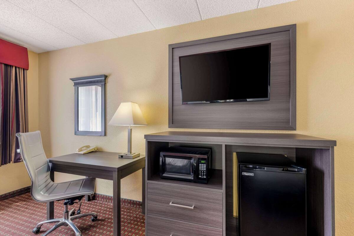 A hotel room with a desk, chair, flat-screen TV, microwave, and mini-fridge.