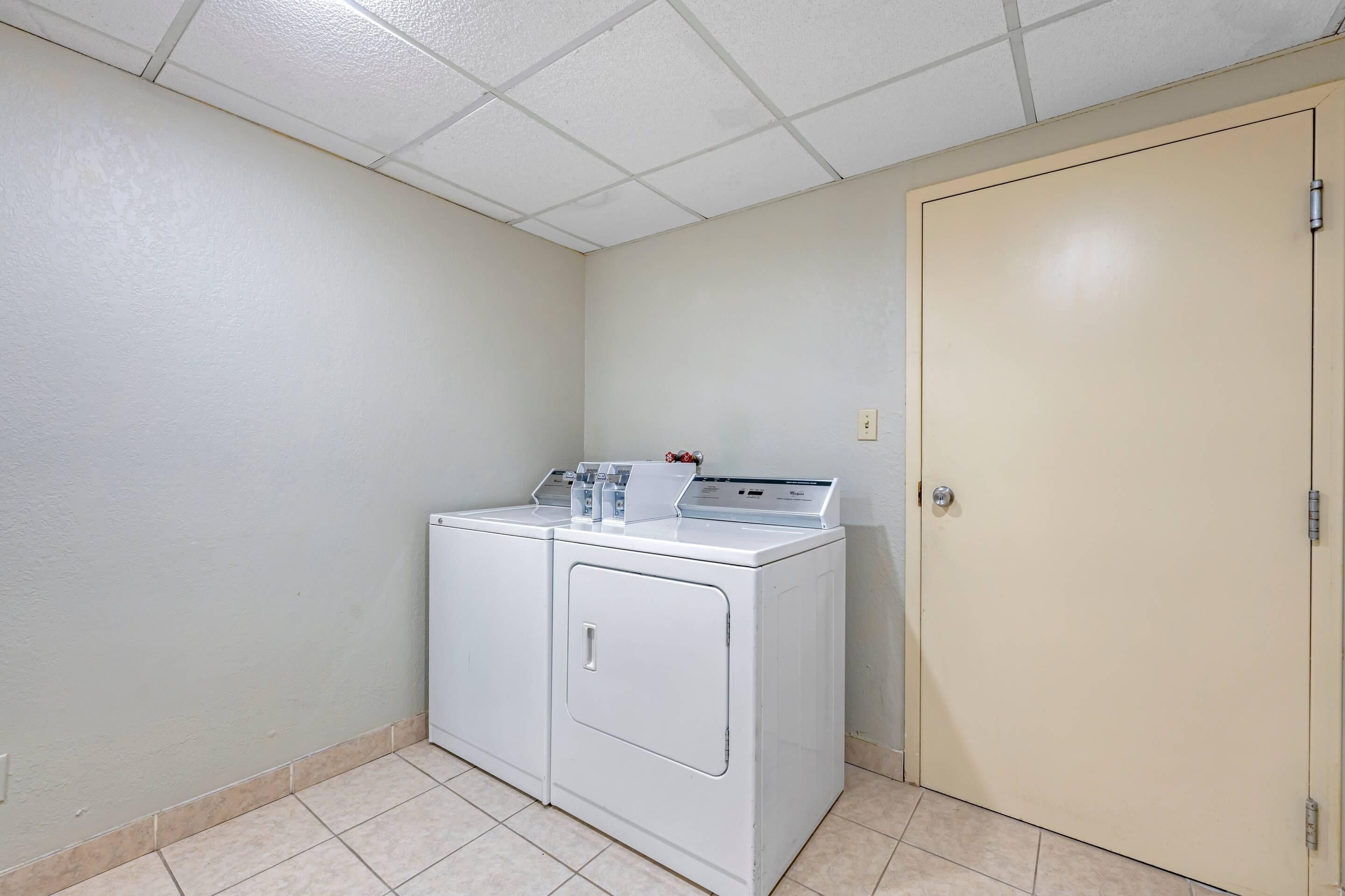 Lavandería con lavadora y secadora de carga frontal, una puerta y piso de baldosas.