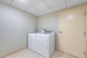 A laundry room with a front-loading washer and dryer, a door, and a tiled floor. - Quality Inn & Suites Lincoln South (Lincoln)