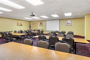 Una sala de conferencias con varias mesas y sillas, un proyector y una pantalla.