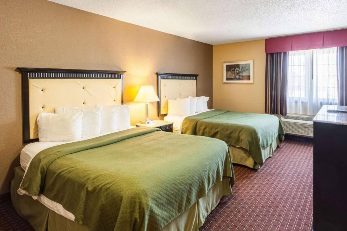 Une chambre d’hôtel avec deux lits, un bureau, une lampe et une fenêtre avec des rideaux.