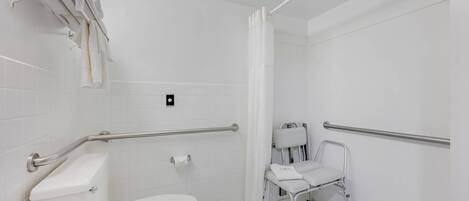 A white bathroom with a toilet, grab bars, a shower area, and a wheelchair-accessible bench.