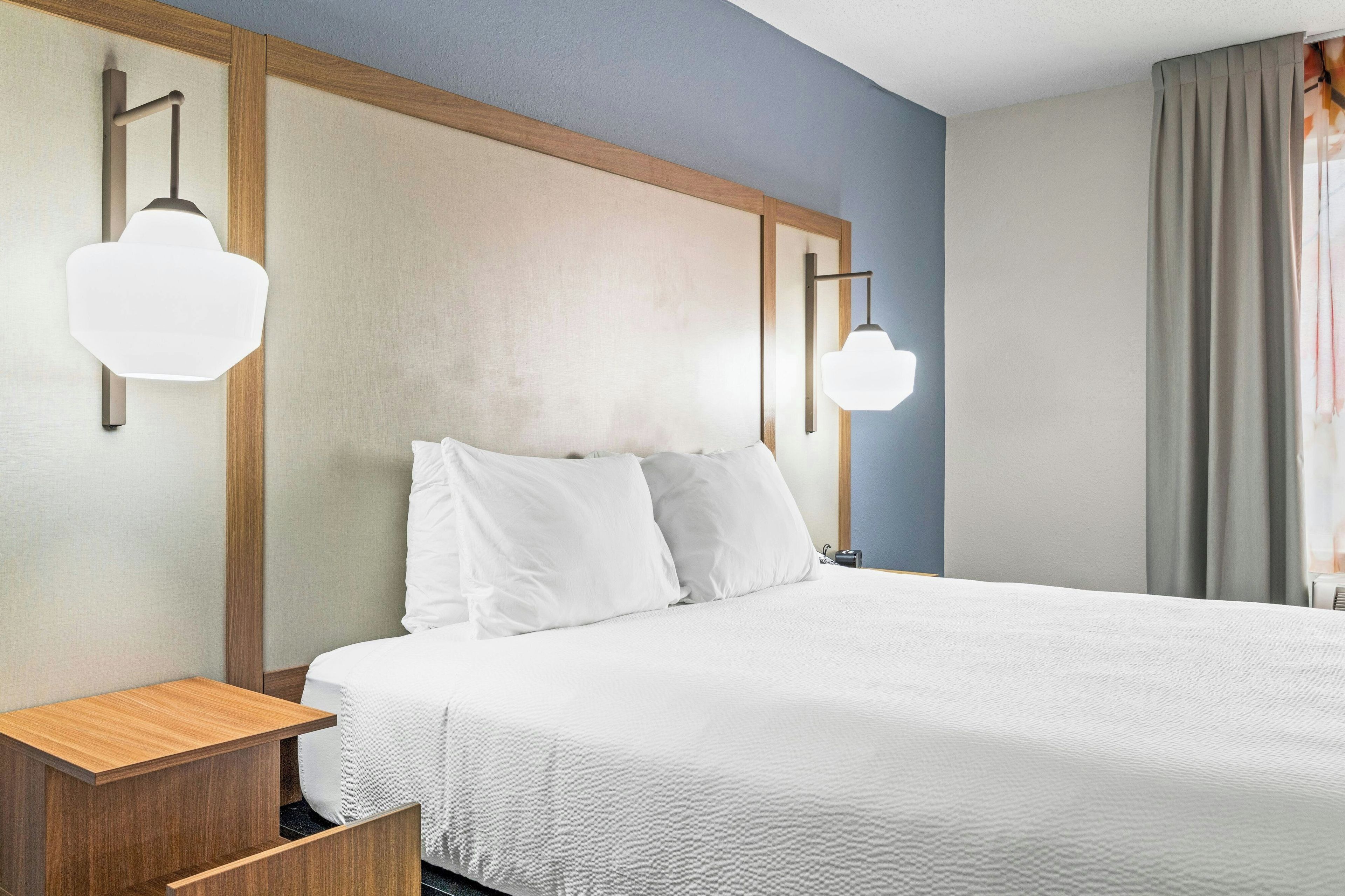 A hotel room with a large bed, two bedside tables, and wall-mounted lights.